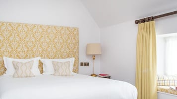 Habitación de hotel con cama, dos lámparas de noche, ventana con cortinas y mesita de noche con lámpara y libro.