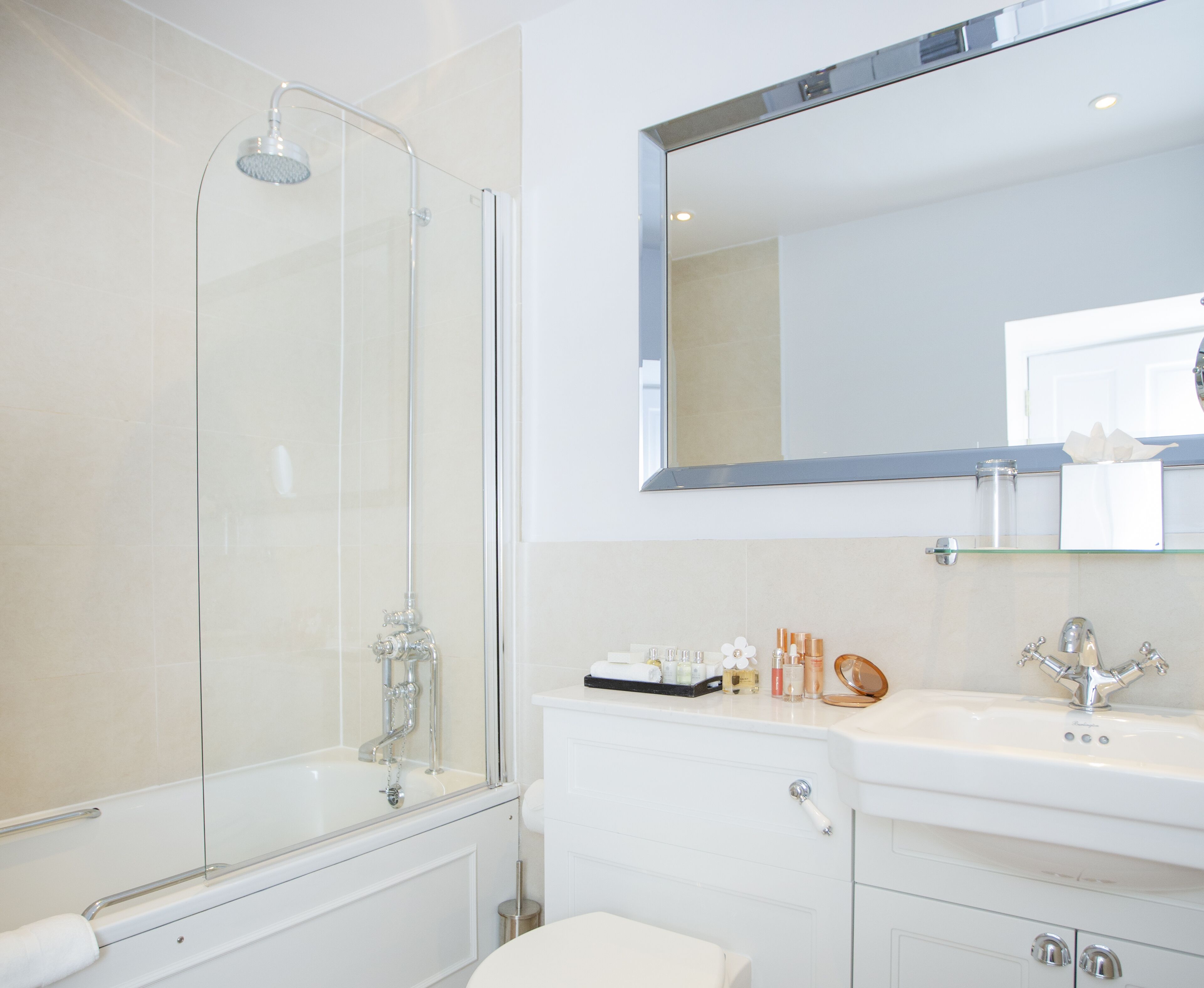 A modern bathroom with a glass-enclosed shower, a white sink with a mirror above, and toiletries on the countertop.