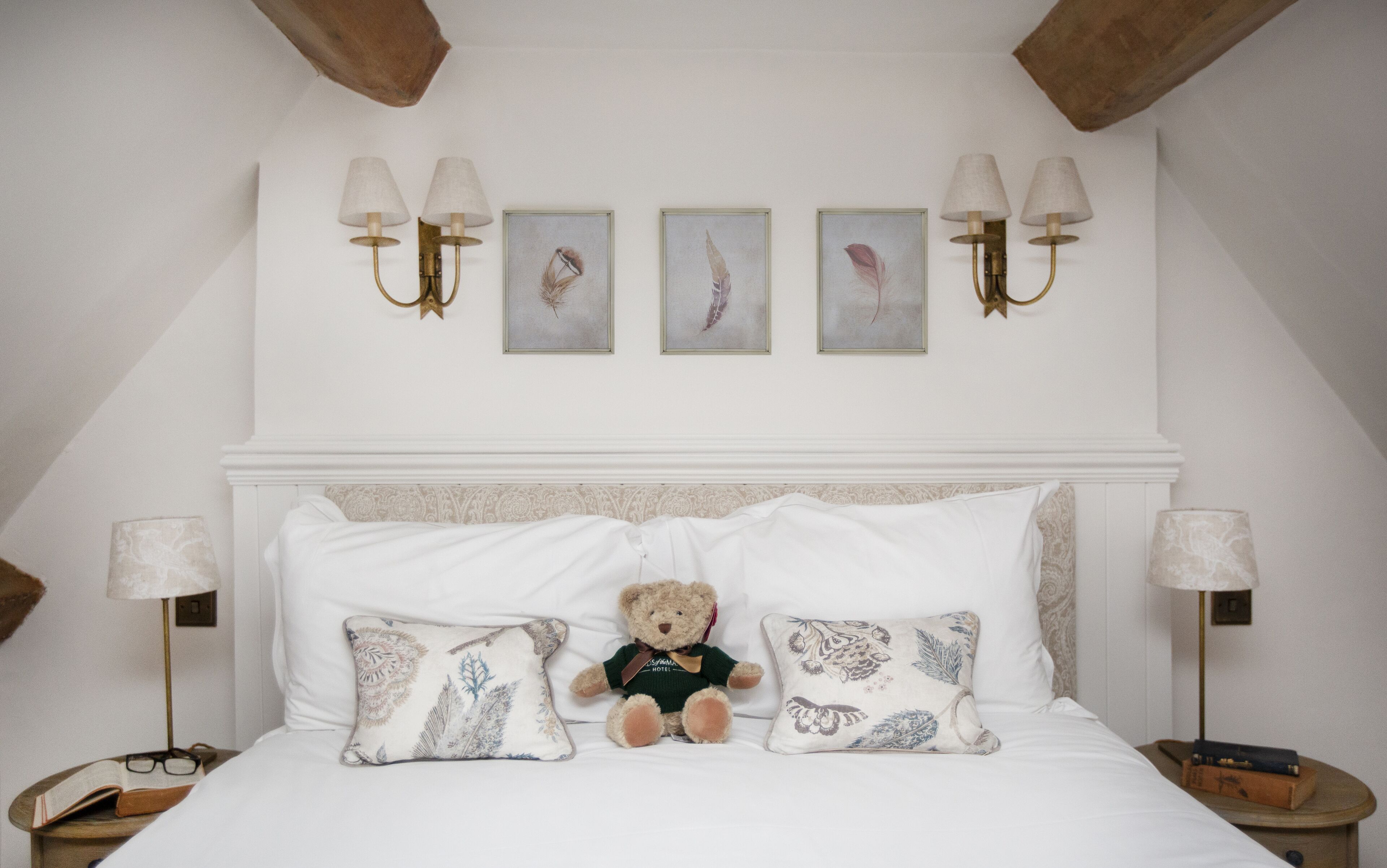 A bedroom with a bed, pillows, a teddy bear, and wall-mounted lamps.
