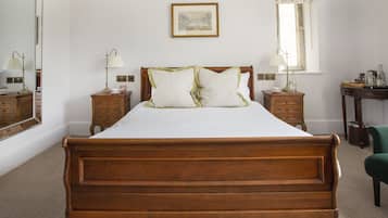 A neatly arranged bedroom with a large wooden bed, two bedside tables with lamps, a framed picture on the wall, and a window with floral curtains.