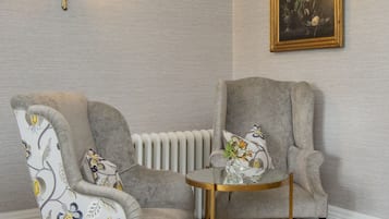 A room with two armchairs, a small round table, a wall-mounted light fixture, and a framed painting.