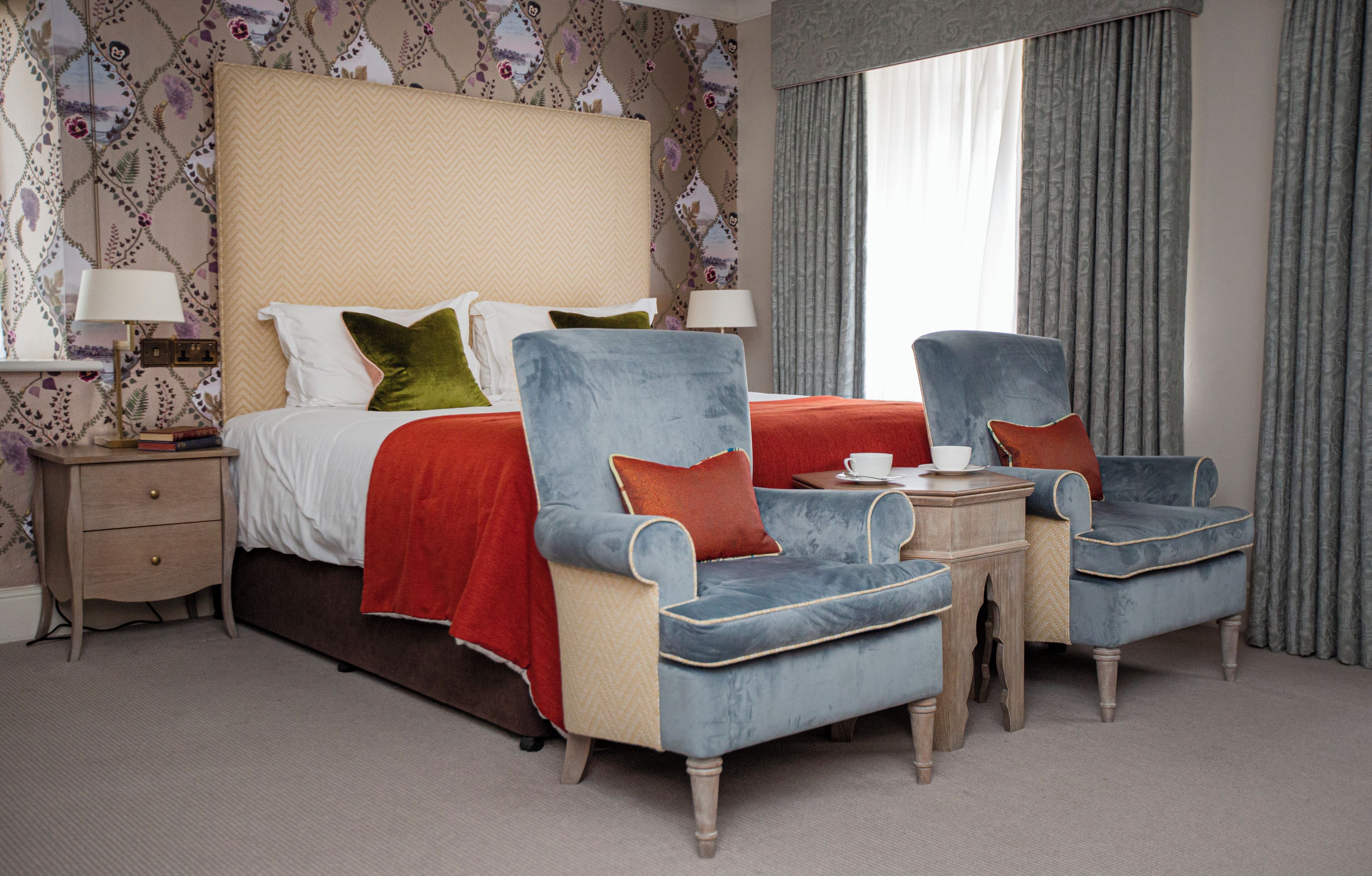 A hotel room with a large bed, two armchairs, a nightstand, and a window with curtains.