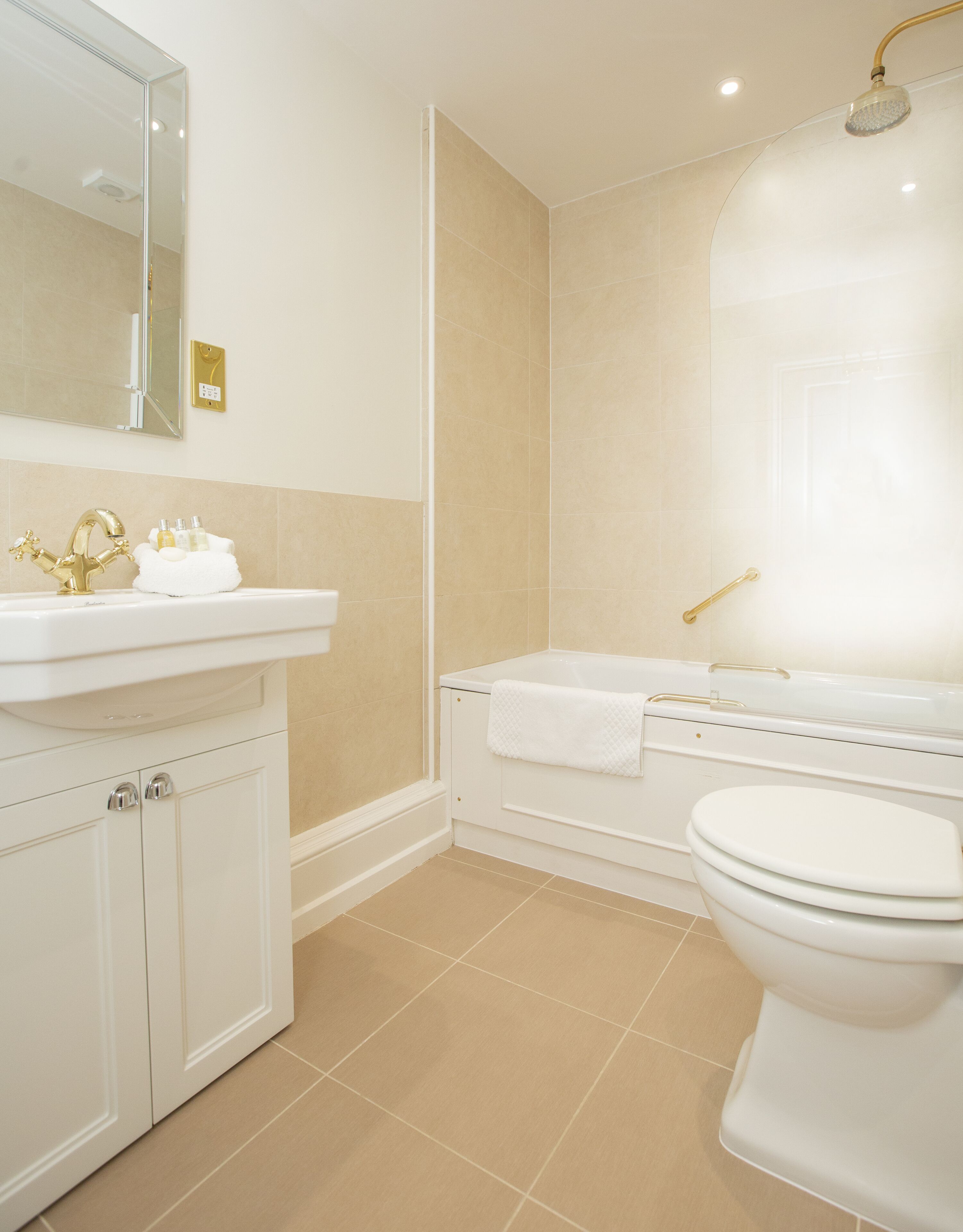 Un baño con lavamanos blanco, grifo dorado y bañera con ducha dorada.