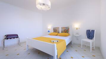 A bedroom with a bed, a bedside table, a chair, a suitcase, and a wall-mounted light fixture.