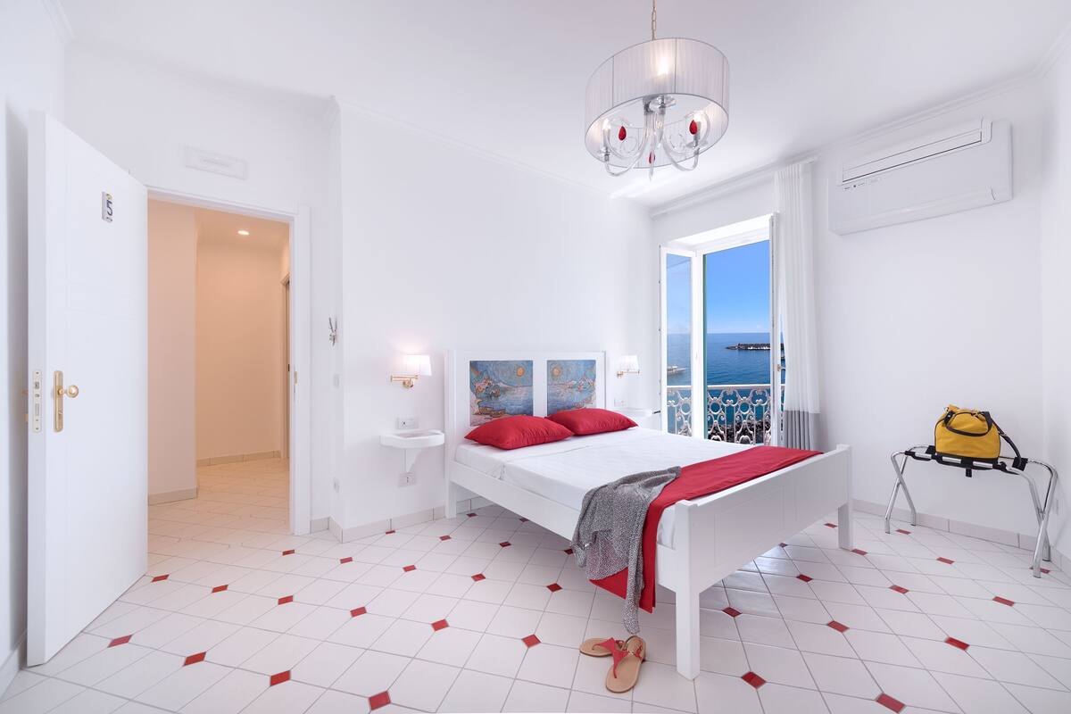 A bedroom with a bed, a window with a view, a bedside table, and a hanging bag.