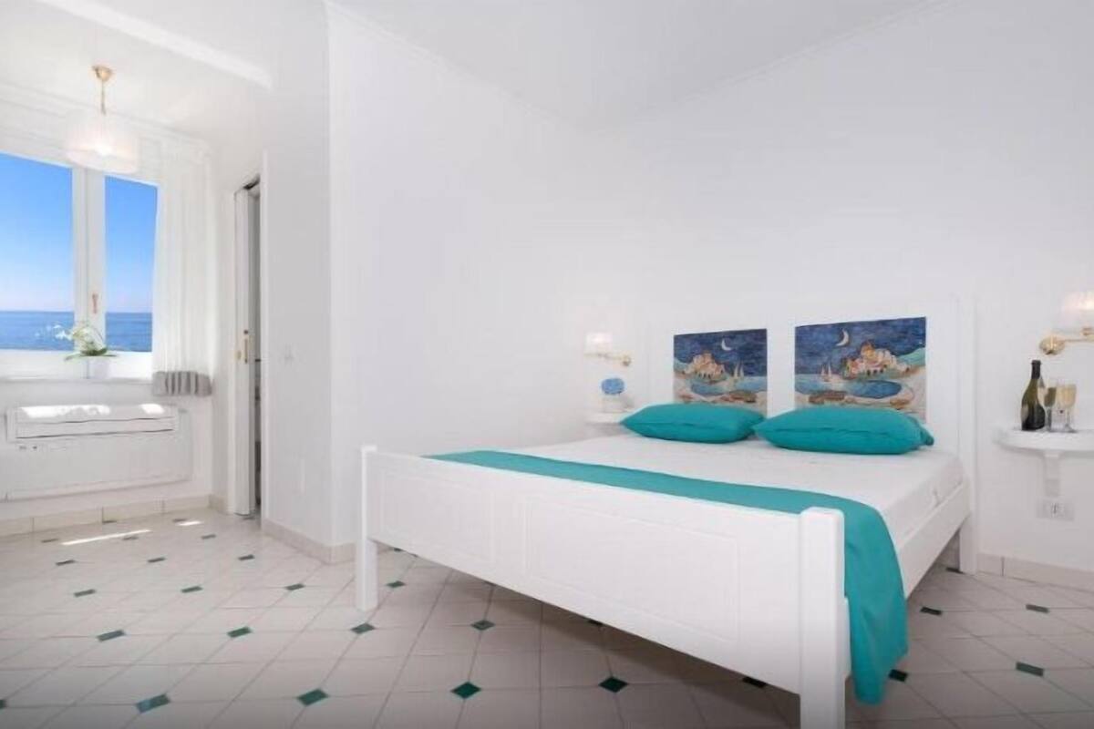 A bedroom with a bed, a window with a view, a radiator, and artwork on the wall.