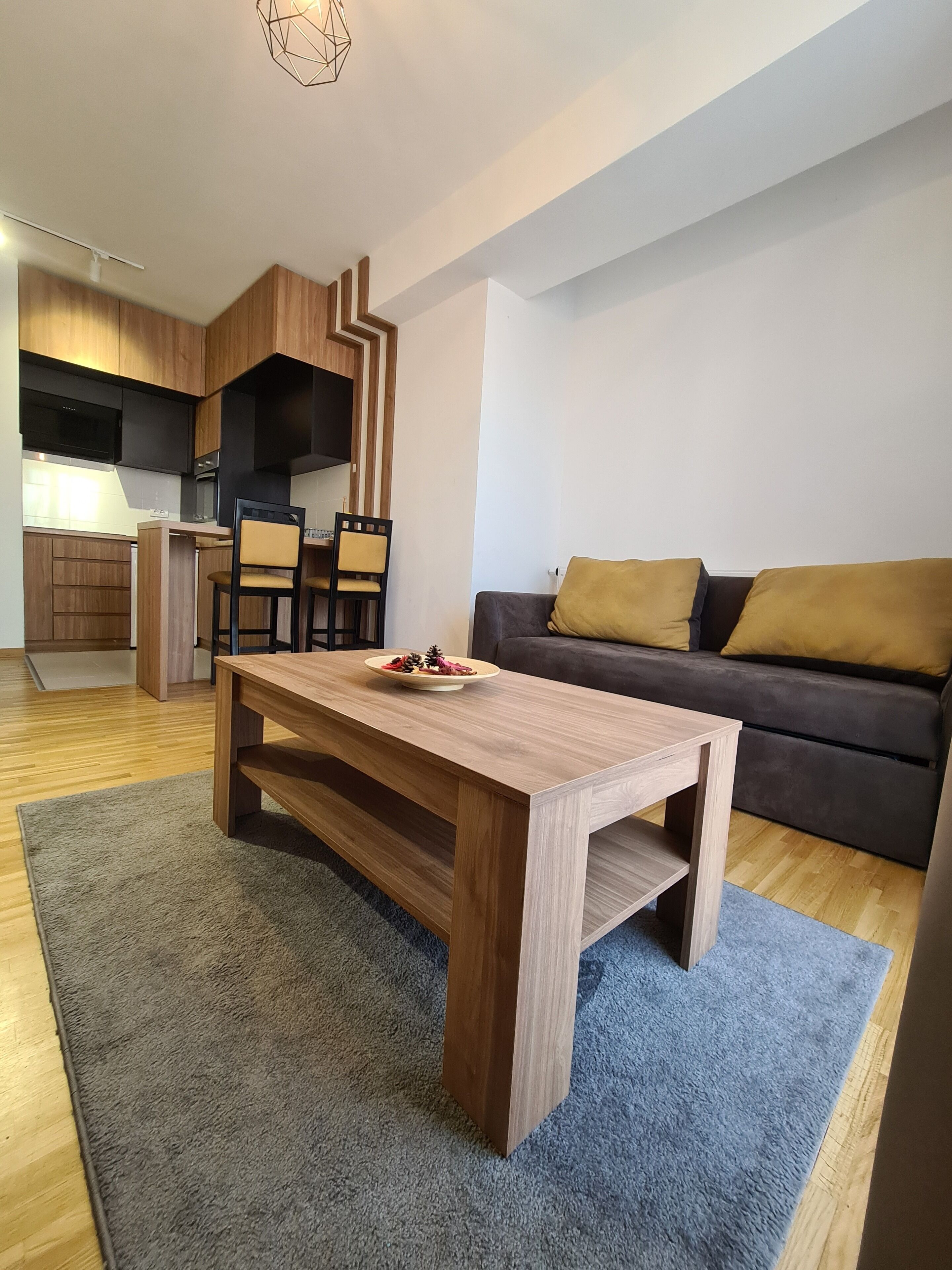 Un soggiorno moderno con un tavolino in legno, un divano con cuscini color senape e un angolo cottura con pensili in legno e forno a incasso.