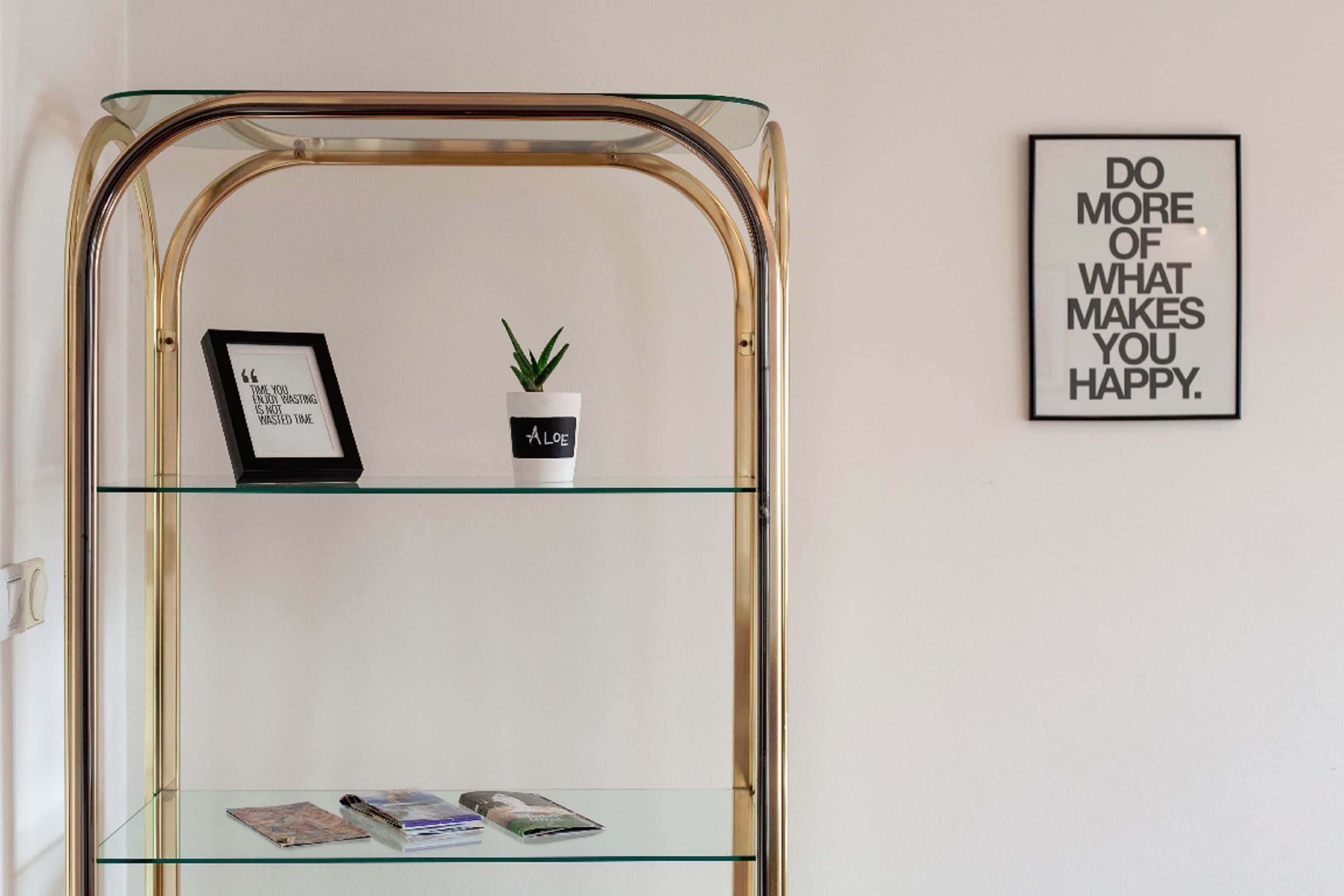 Een glazen displayplank met een ingelijste citaat, een kleine potplant en tijdschriften.