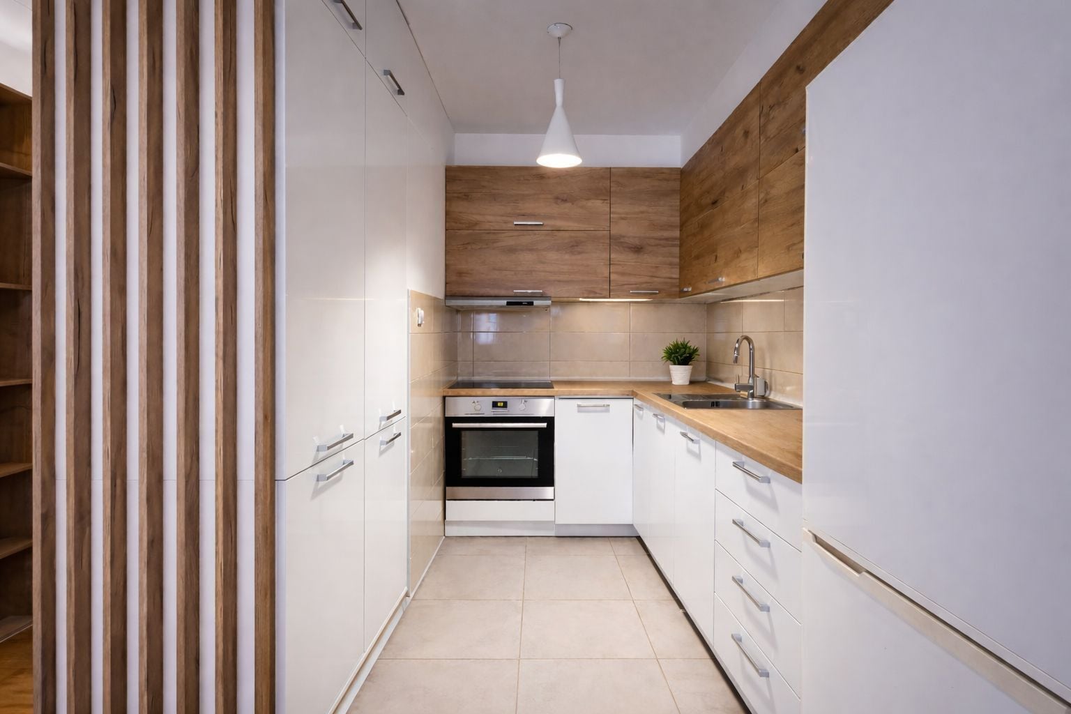 A modern kitchen with white cabinetry, a wooden accent wall, a built-in oven, and a sink.