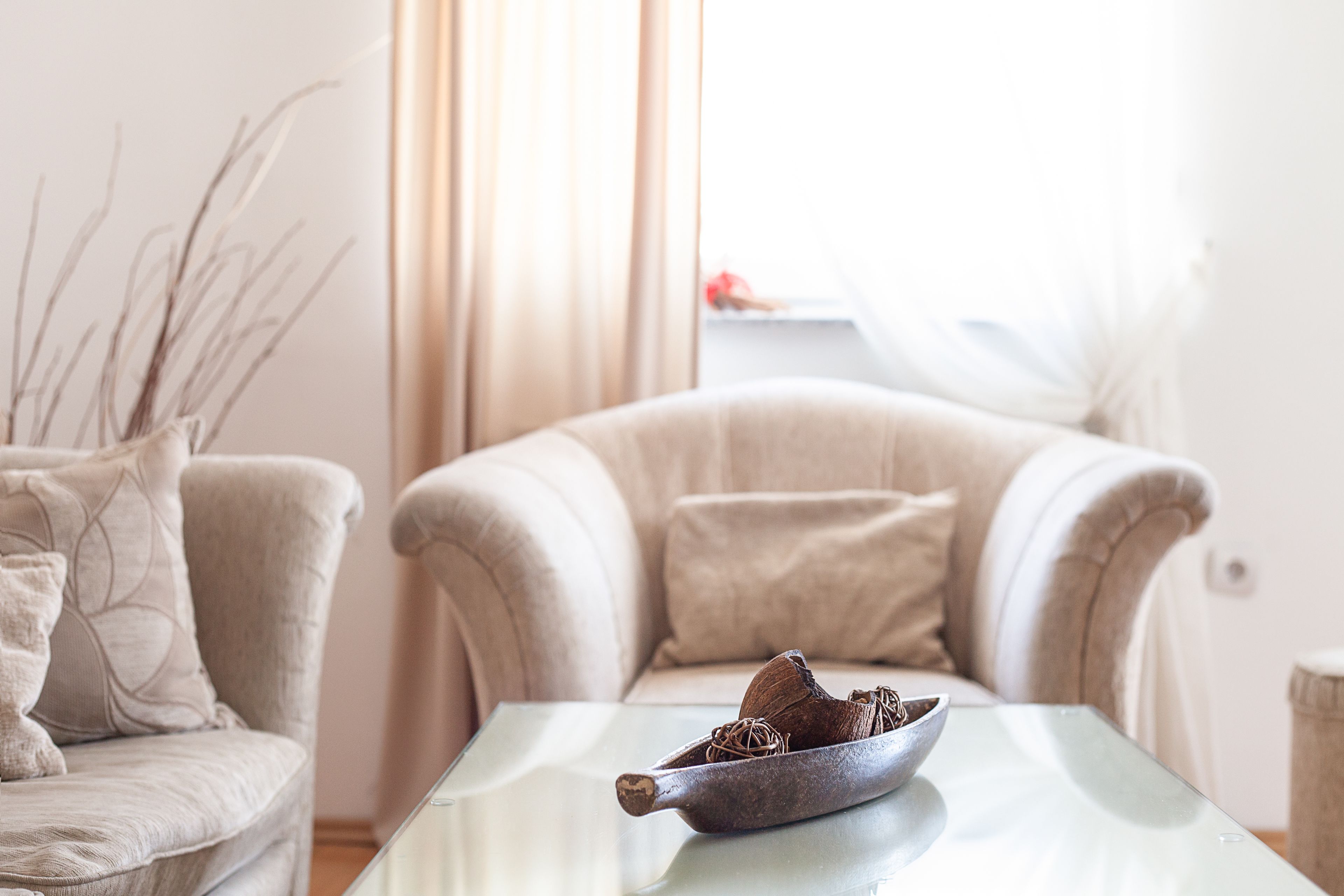 A living room with a glass coffee table, a beige armchair, and a vase with branches.