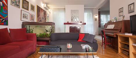 Ein Wohnzimmer mit einem roten Sofa, einem schwarzen Sofa mit roten Kissen, einem Holztisch, einem Aquarium und einem Klavier.