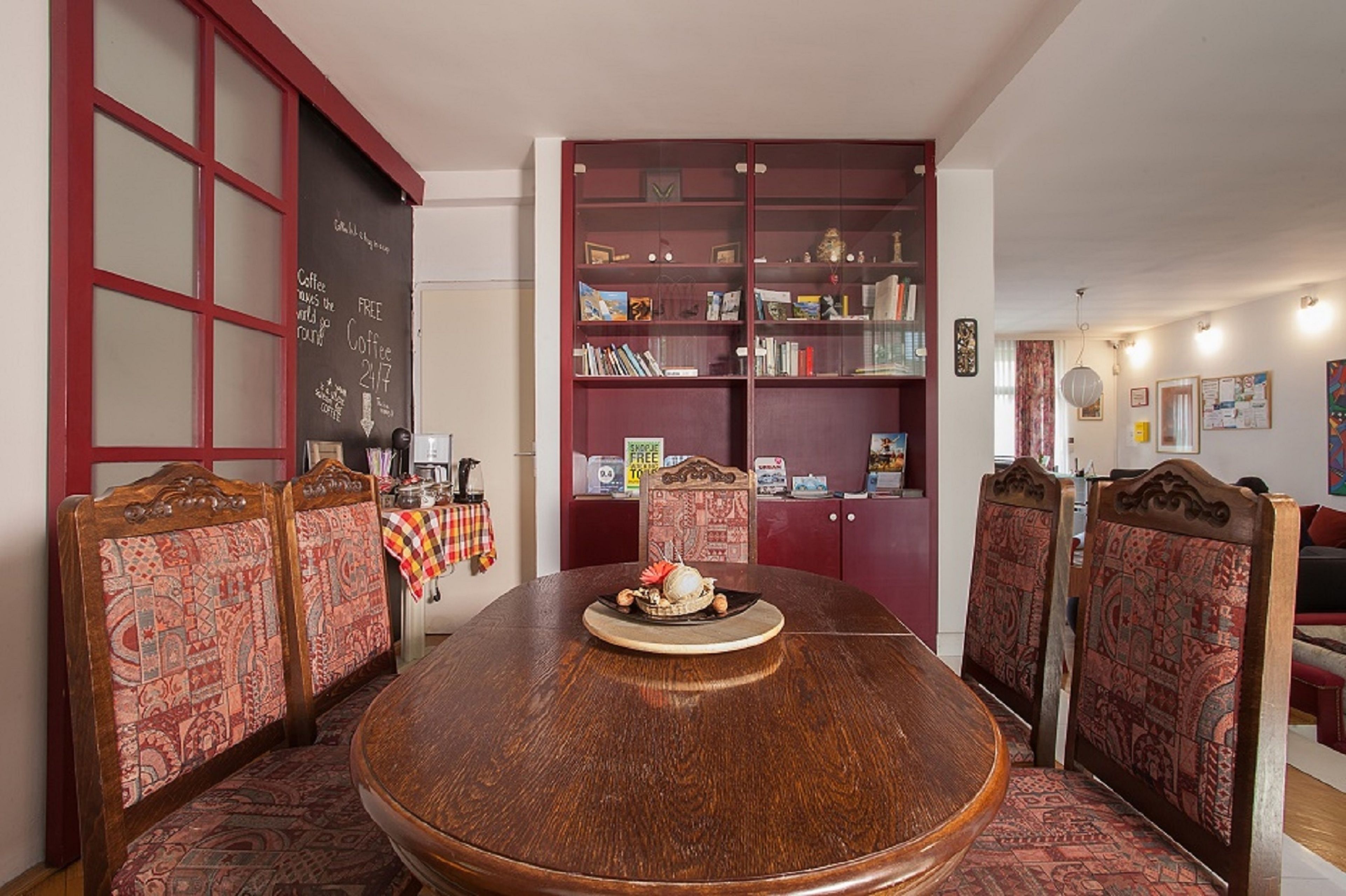 A dining area with a round wooden table, patterned chairs, and a bookshelf filled with books and decorative items.