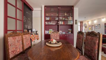 A dining area with a round wooden table, patterned chairs, and a bookshelf filled with books and decorative items.