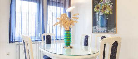 A dining area with a glass table, white chairs, and a vase with flowers.