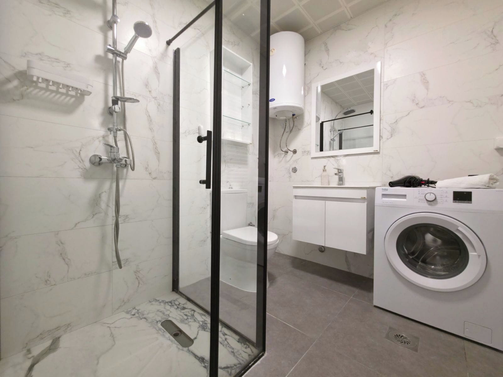 A modern bathroom with a glass-enclosed shower, a toilet, a washing machine, and a sink with a mirror above it.