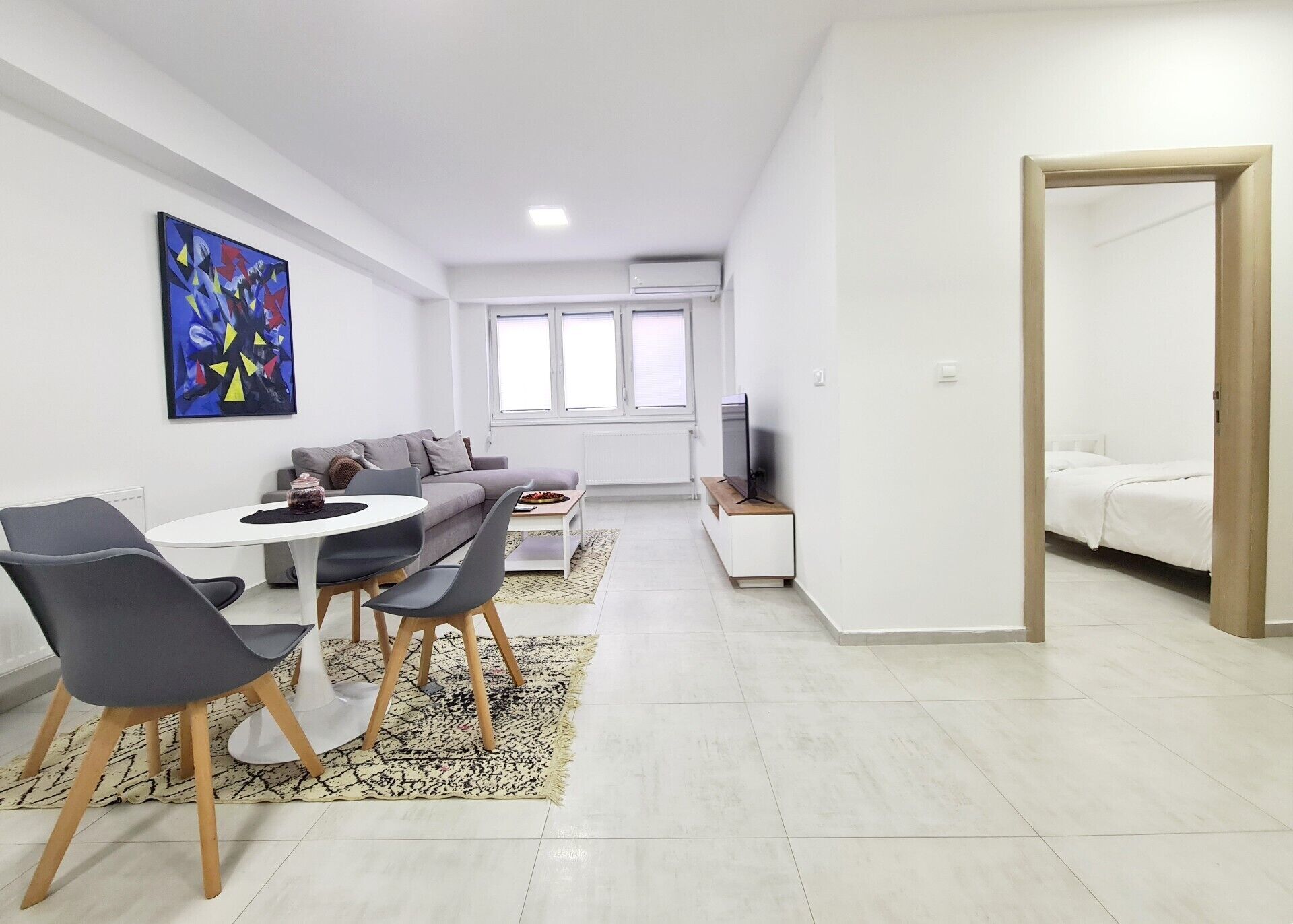 A modern living room with a dining area, a sofa, a TV, and a large window.