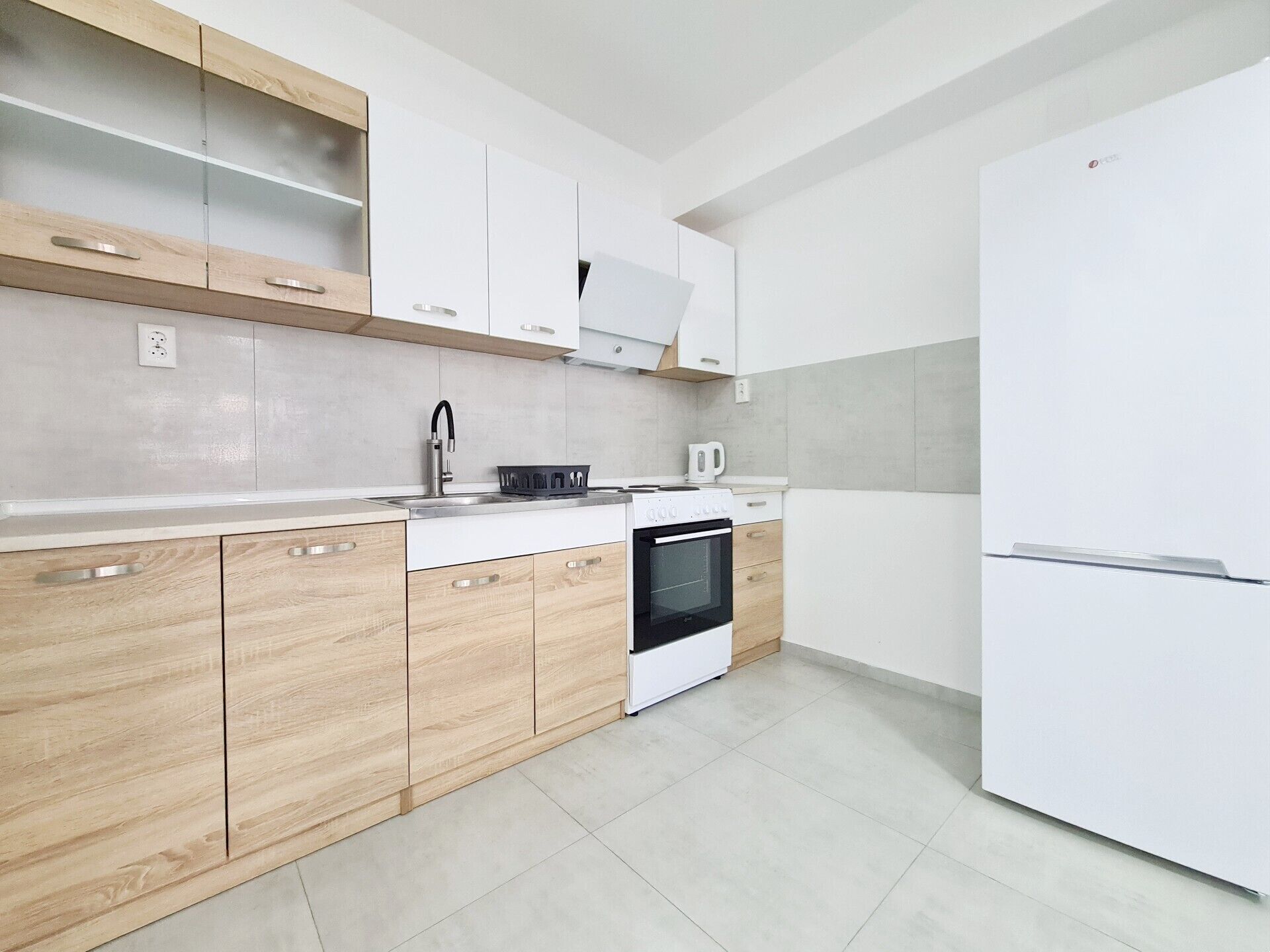 A modern kitchen with wooden cabinets, a built-in oven, a white refrigerator, and a stainless steel sink.
