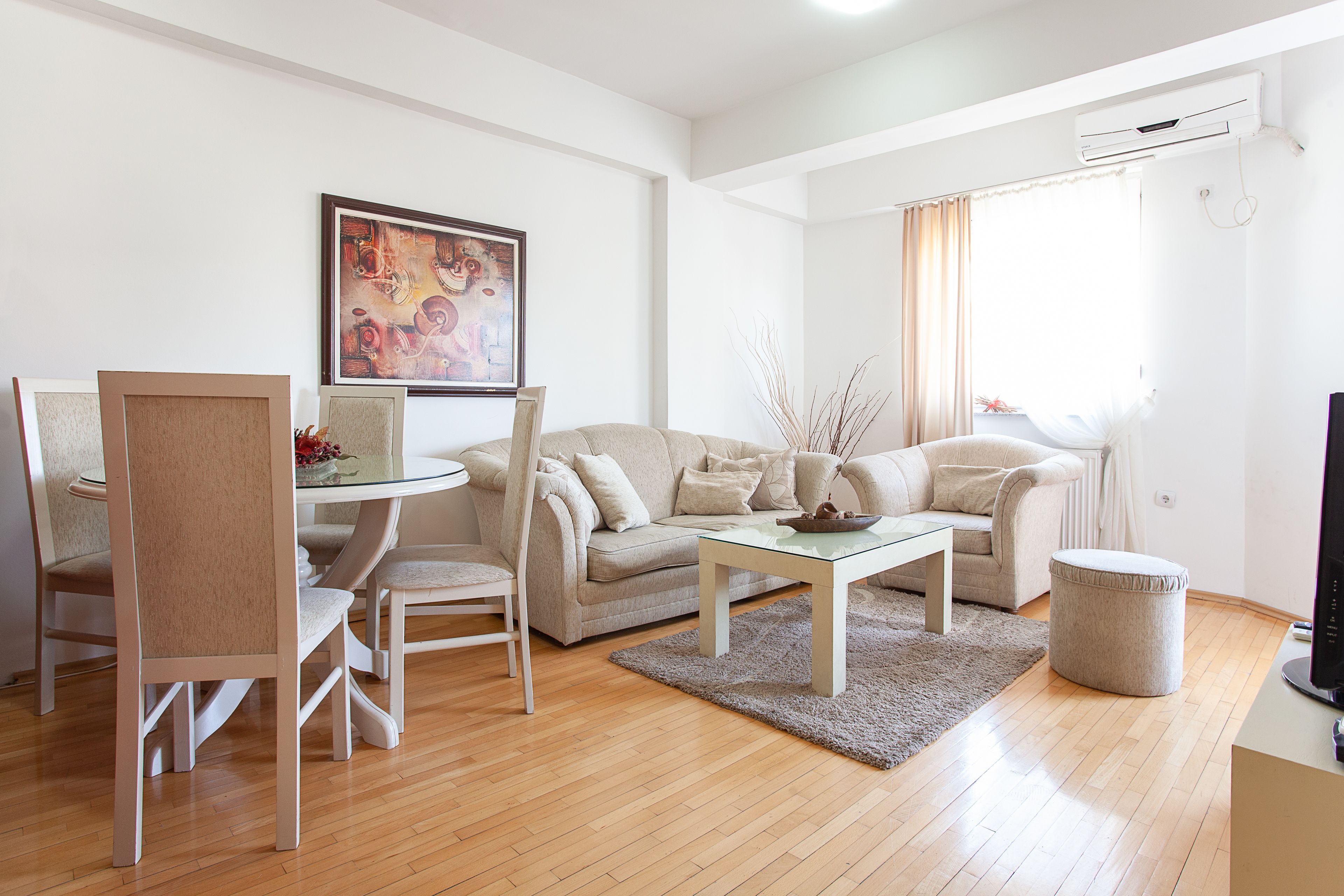 Un salon moderne avec un canapé beige, une table basse en verre et un coin repas comprenant une table et des chaises blanches.