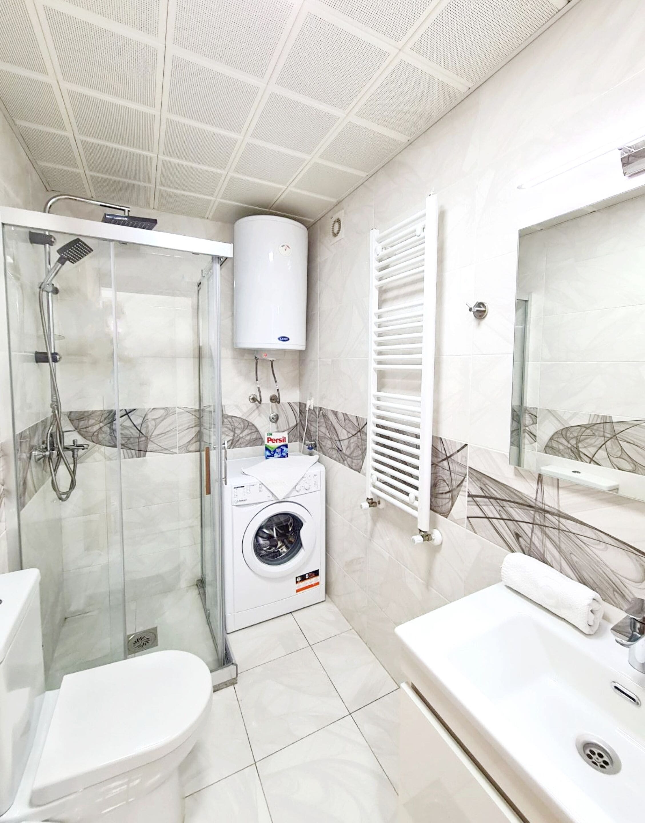 Een moderne badkamer met een douchecabine, een ingebouwde wasmachine, toilet en bad.