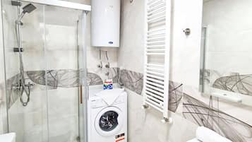 A modern bathroom with a glass-enclosed shower, a built-in washing machine, a toilet, and a bathtub.
