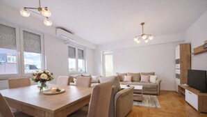 A modern living room with a wooden dining table, beige sofa, and a TV on a wooden stand. - Urban Serviced Apartments (Skopje)