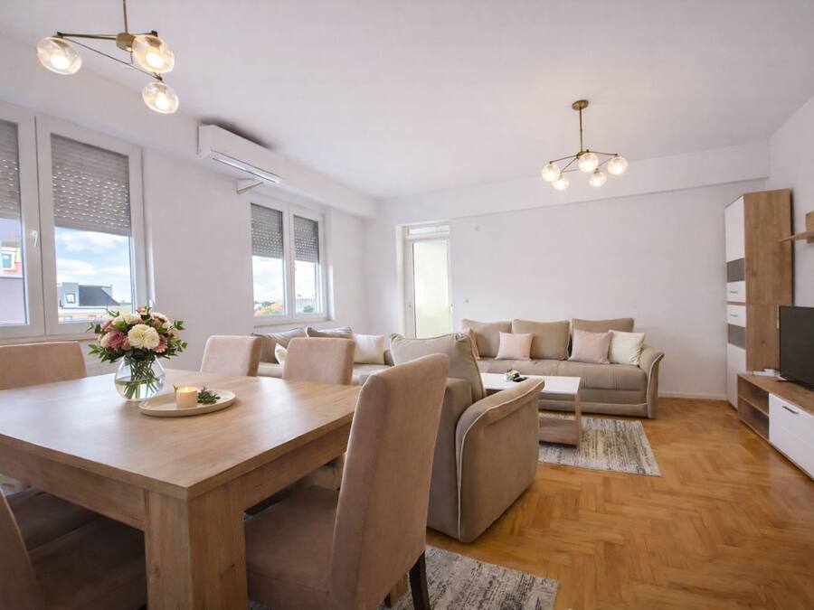 Una sala moderna con una mesa de comedor de madera, un sofá color crema y un televisor sobre un mueble de madera.