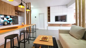 A modern apartment with a kitchen, dining area, and living room. It includes a wooden bar, a sofa, and a TV mounted on the wall. - Urban Serviced Apartments (Skopje)