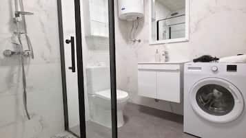 Un baño con ducha de vidrio, inodoro, lavabo con espejo y lavadora.