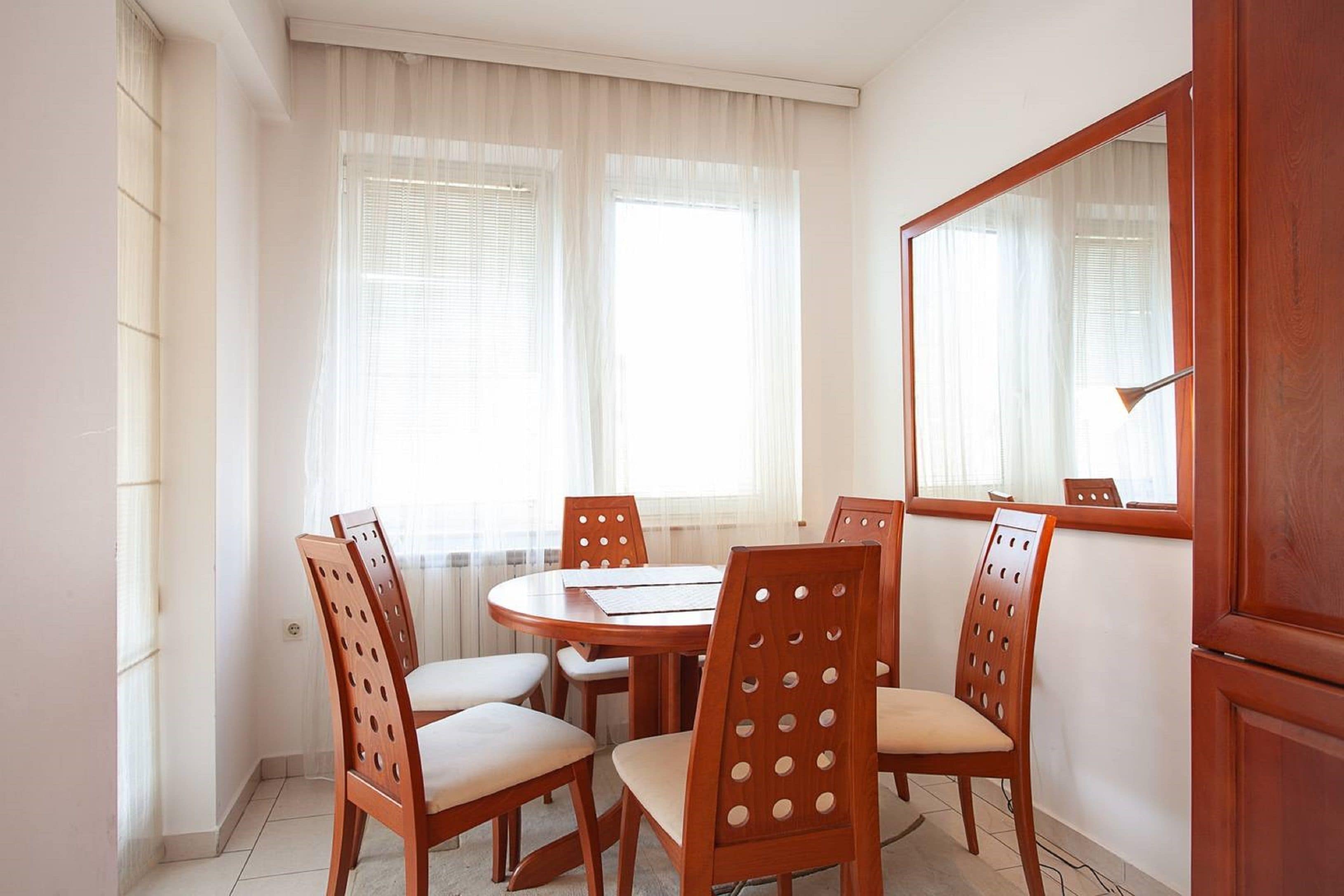 A dining area with a round table and six wooden chairs with cut-out backrests.