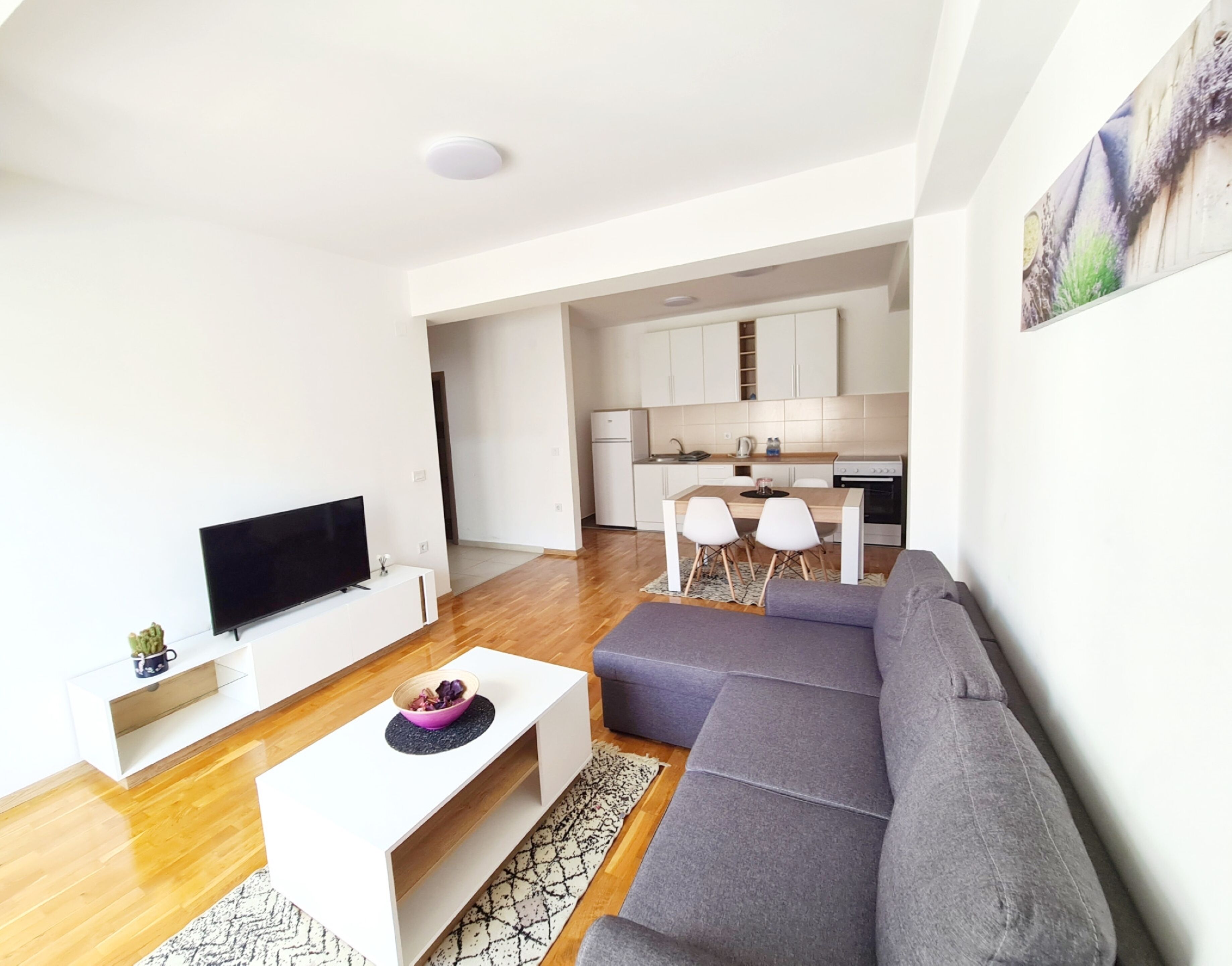 A modern living room with a flat-screen TV, a gray sofa, and a white coffee table.