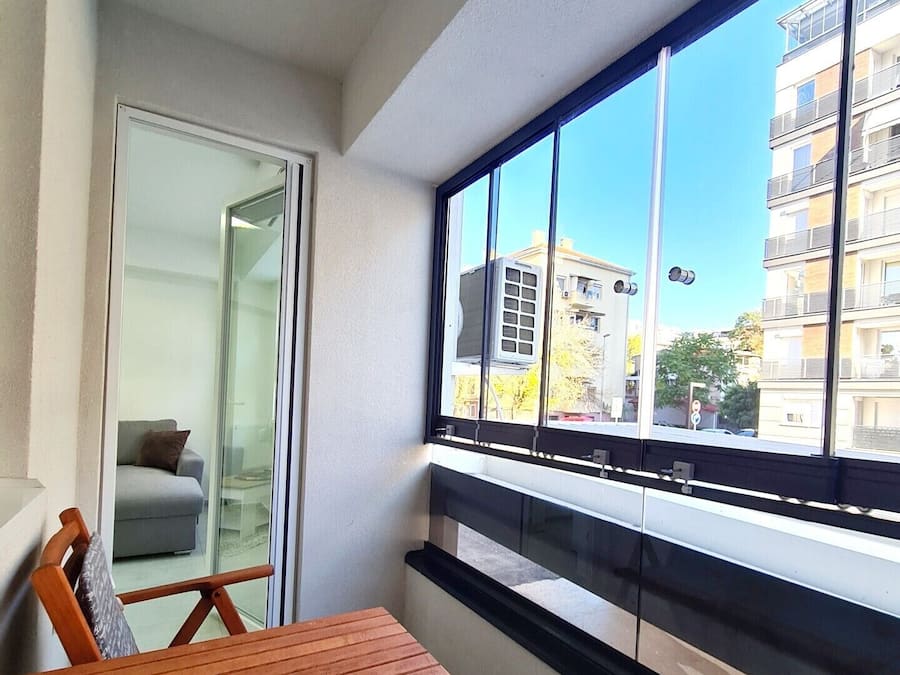 A balcony with a wooden table and chairs, a sliding glass door leading to a living area, and a view of a building and trees.