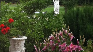 A garden with a statue, a stone urn, and flowering plants. - Chateau du Mesnil (La Vieille-Lyre)