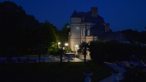 A large, two-story building with a prominent tower and a balcony. The building is surrounded by a well-maintained garden with palm trees and a paved patio area with outdoor seating. - Chateau du Mesnil (La Vieille-Lyre)