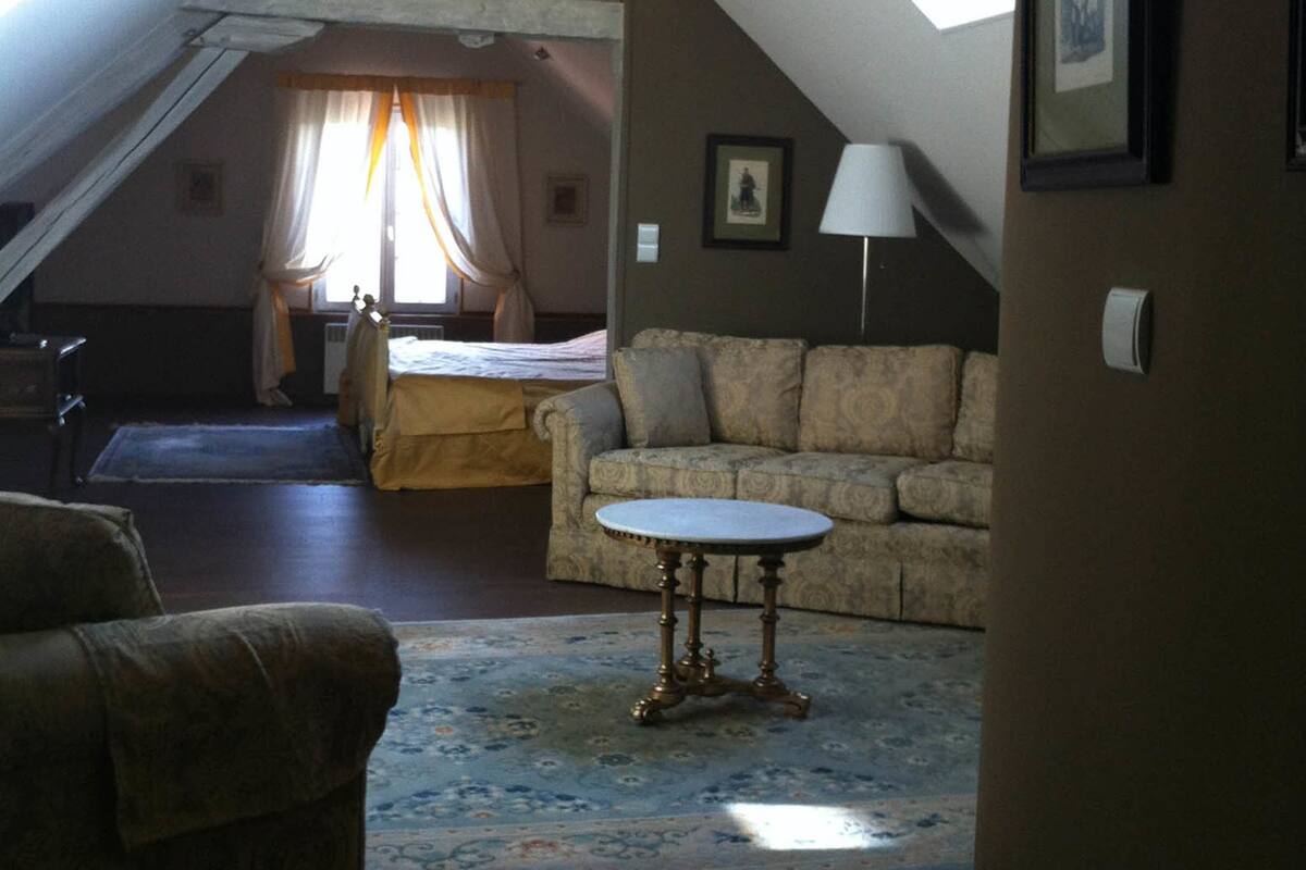 Een zolderkamer met hoge plafonds, een schuine kap, een bed, een slaapbank en een kleine tafel.