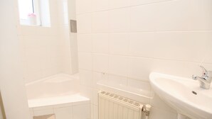 Un baño con azulejos blancos, una bañera, un lavamanos y una ventana con un objeto rosa.
