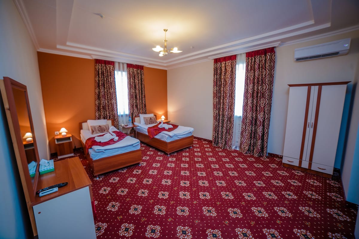 Habitación de hotel con dos camas, un armario, un escritorio con lámpara y suelo alfombrado.