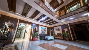 A spacious lobby with a high ceiling, a central seating area, and a staircase leading to an upper level. - Arkanchi Hotel (Khiva)