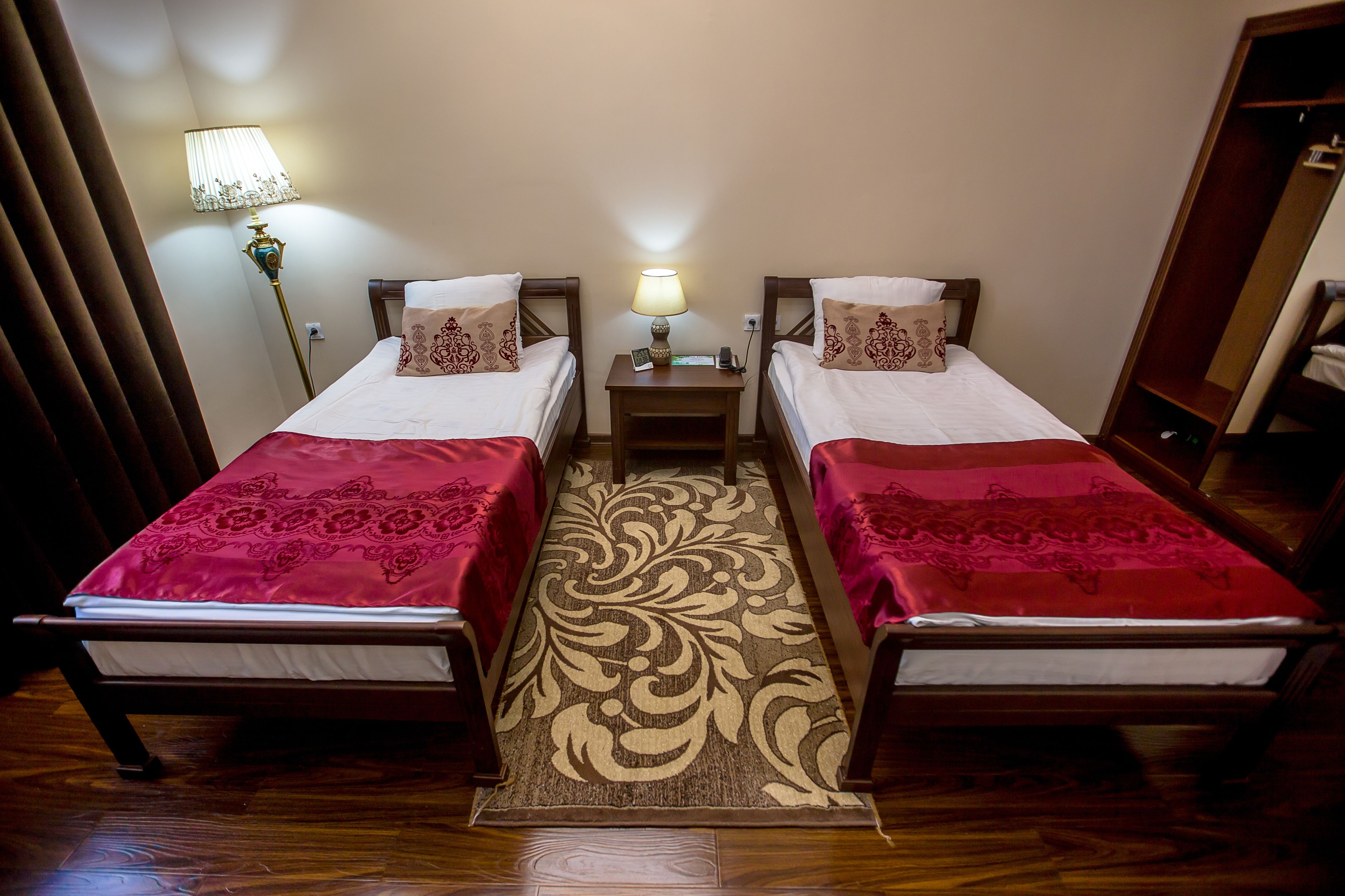 A hotel room with two single beds, a nightstand with a lamp, and a wooden floor.