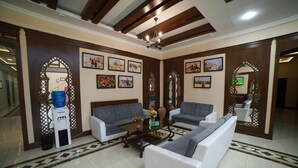 A spacious living room with a high ceiling, wooden beams, and a tiled floor. There are two sofas, a coffee table, and a water dispenser. - Arkanchi Hotel (Khiva)