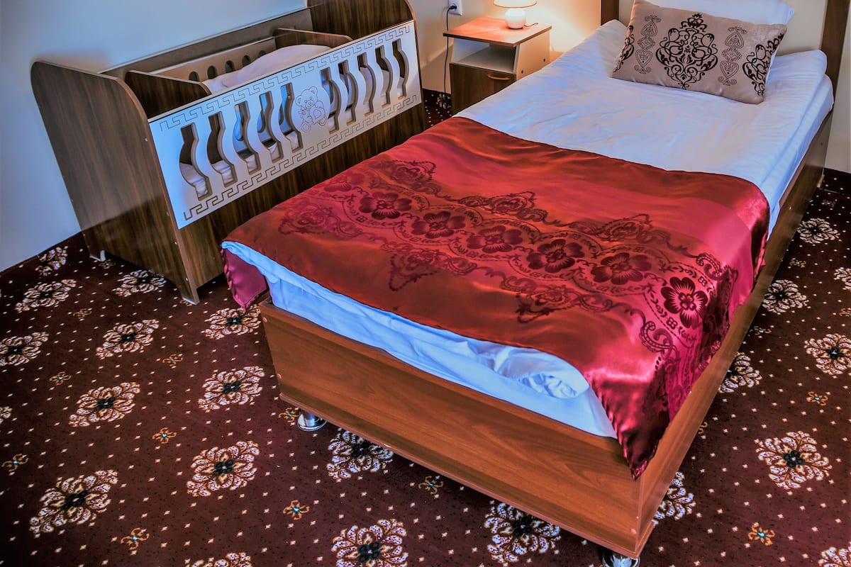 Una cama bien hecha con una colcha roja estampada, un cabecero de madera y una lámpara de noche.