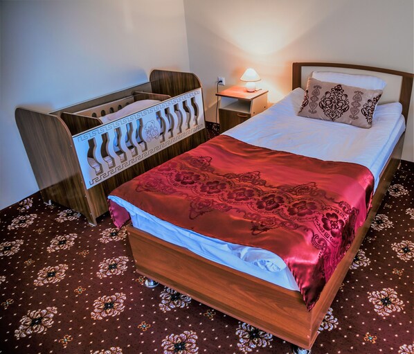 A neatly made bed with a red patterned bedspread, a wooden headboard, and a bedside lamp. - Khan Hotel Khiva (Khiva)