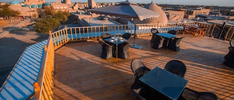 A rooftop terrace with outdoor seating, a pool, and views of a cityscape including a mosque and minaret.