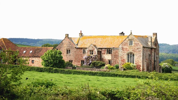 A large stone building with a traditional architectural style, surrounded by lush green fields and hills in the background. - Blackmore Farm (Bridgwater)