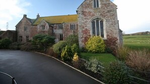 A stone building with a prominent tower and a large arched window, surrounded by greenery and a paved driveway. - Blackmore Farm (Bridgwater)