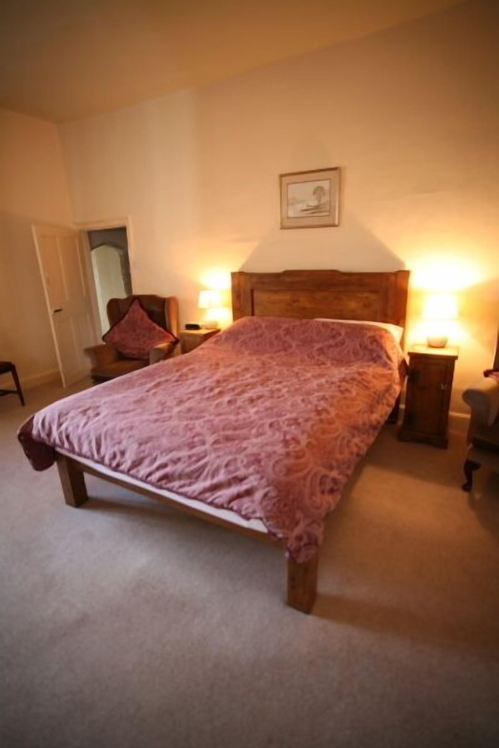 A bedroom with a large bed, two bedside tables with lamps, a chair, and a door.