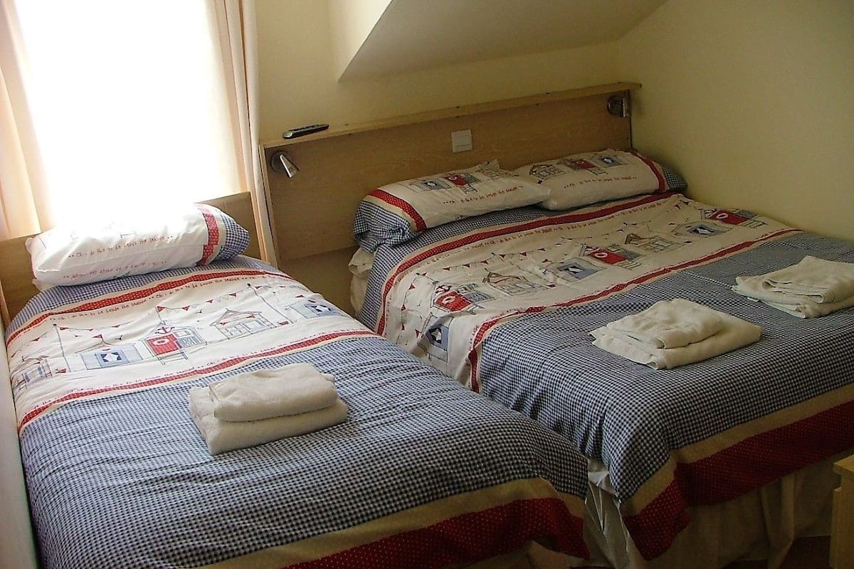 Two single beds with checkered bedding and towels, a wooden headboard, and a window with curtains.