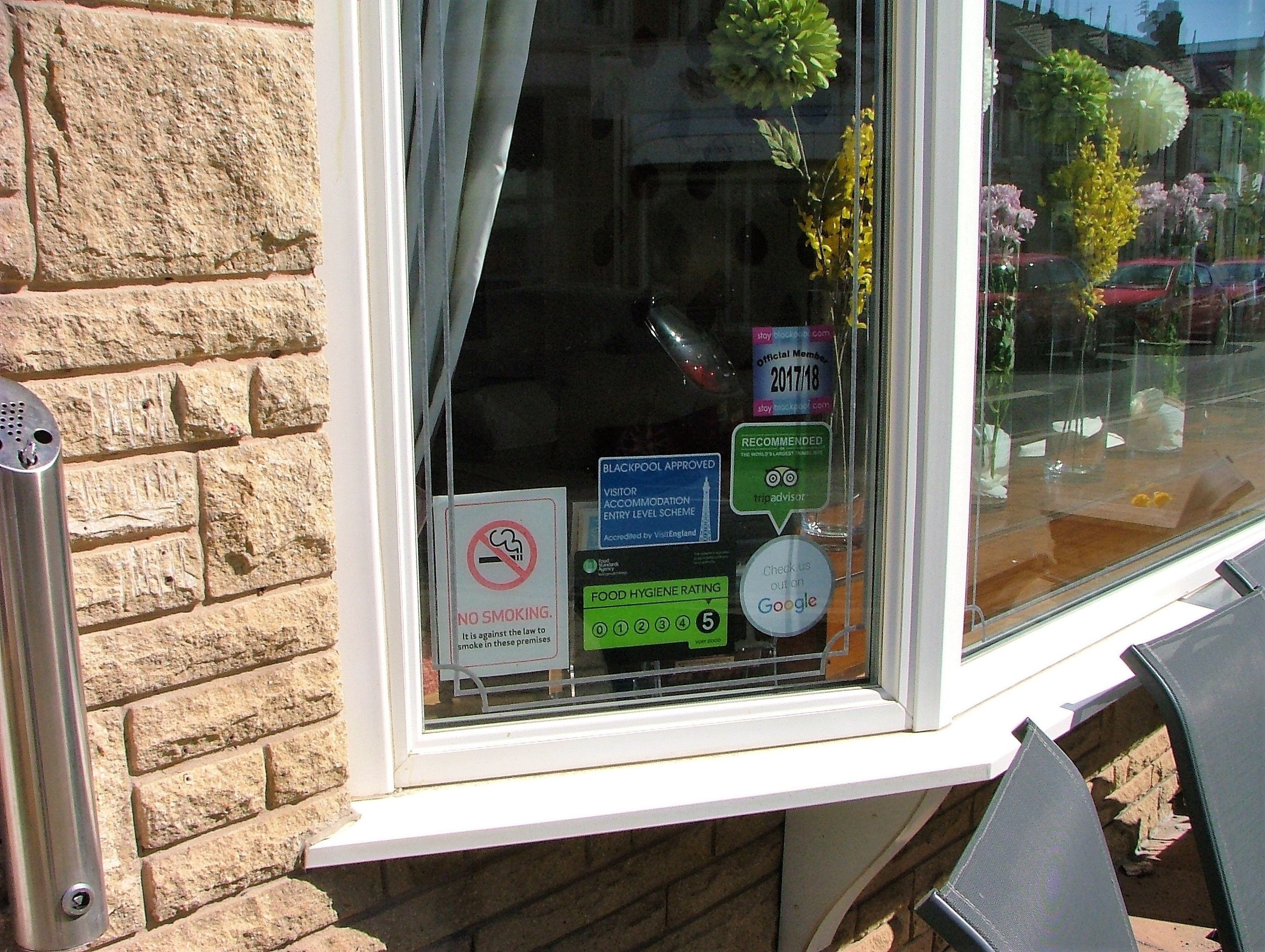 A window with various stickers including a no smoking sign, a food hygiene rating, and a Google check-out option.