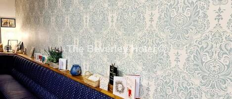 Un área de recepción con un papel tapiz estampado, un mostrador de madera y un banco tapizado en azul.