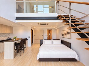 Une chambre moderne avec un grand lit, un bureau avec des chaises et un escalier.