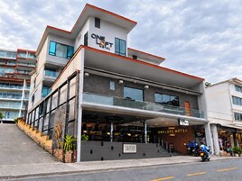 A modern hotel with a glass facade, a visible restaurant named 'SUZEUS,' and a sign for 'ONE LOFT HOTEL.'